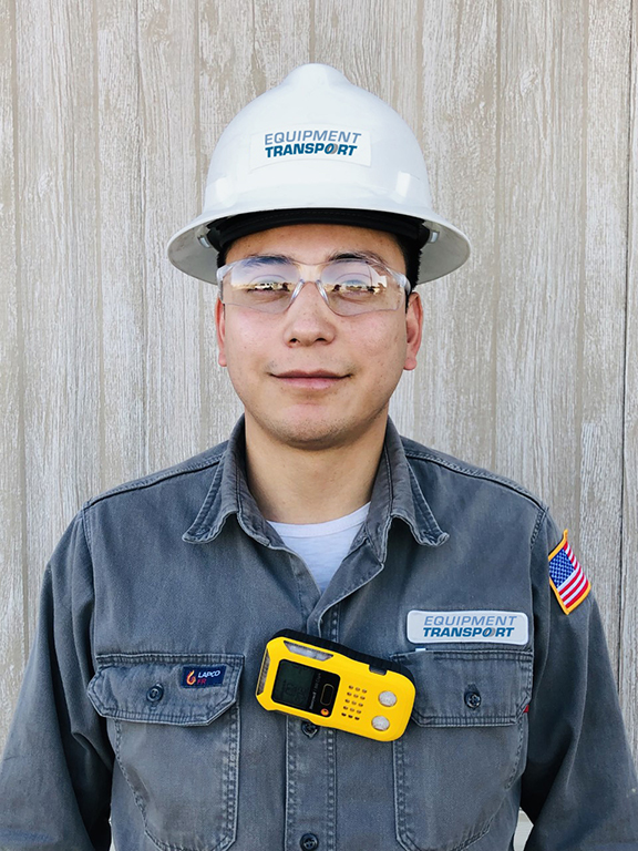 Image of an Equipment Transport truck driver employee wearing a monitoring device, safety glasses, and fire retardant apparel. Equipment Transport is a leading provider of midstream logistics solutions.