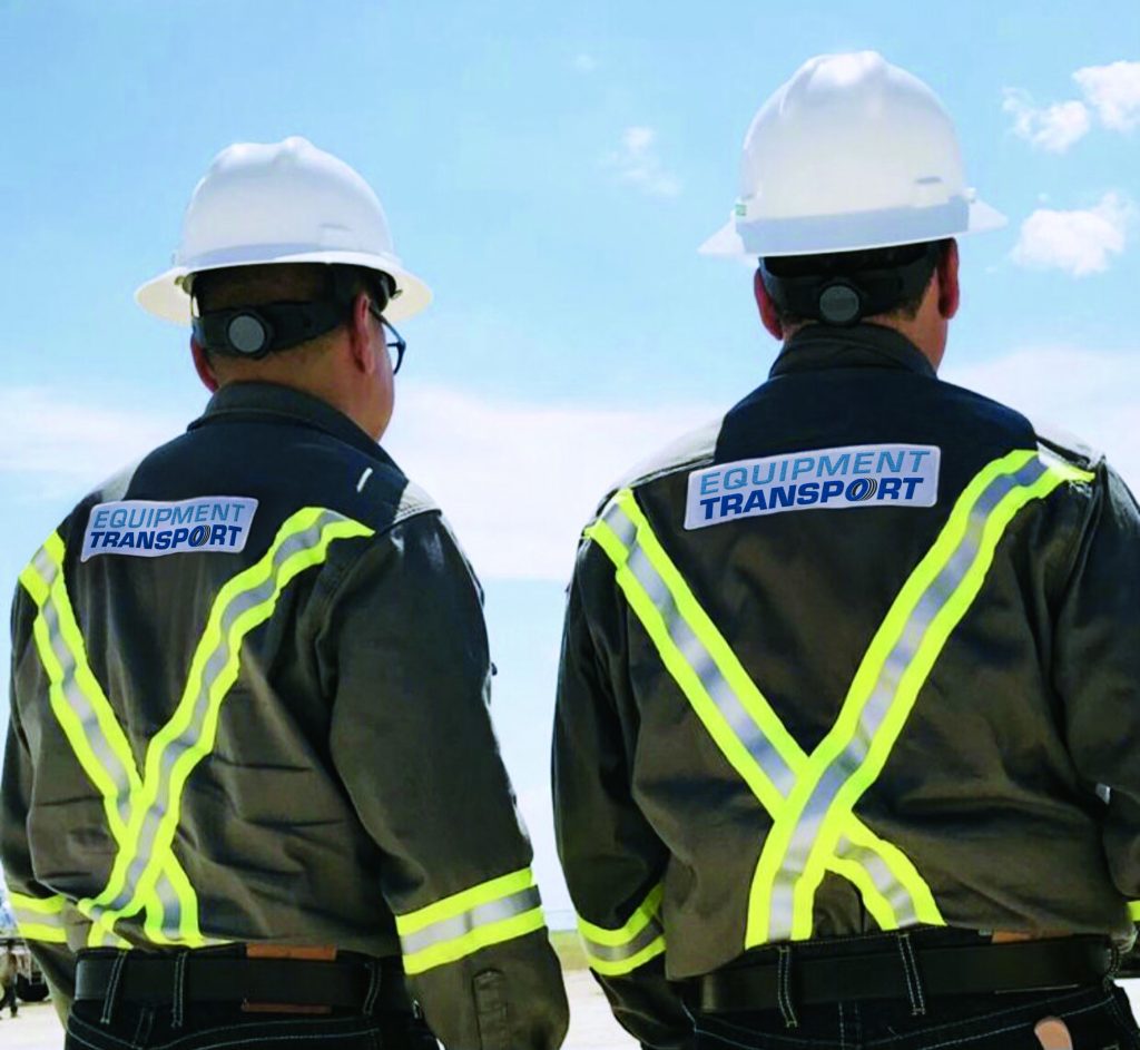 Image of two Equipment Transport employees wearing hard hats, safety glasses, and reflective fire retardant jackets. Equipment Transport is a leading provider of midstream logistics solutions.