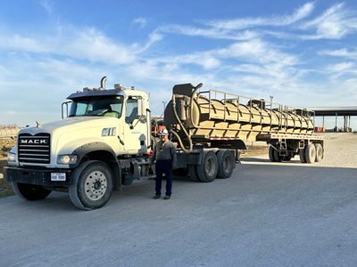 Image of an Equipment Transport truck with an employee standing in front wearing a hardhat. Equipment Transport is a leading provider of midstream logistics solutions.